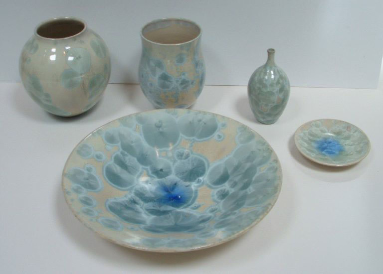 A collection of crystalline pottery art with white vases and dishes coated by blue crystalline glazes.